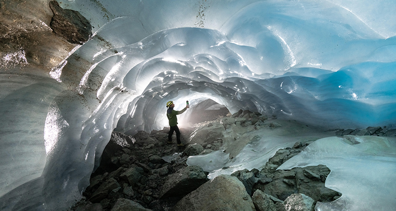 a-man-crouched-down-inside-the-vast-gorner-glacier-cave-800x428