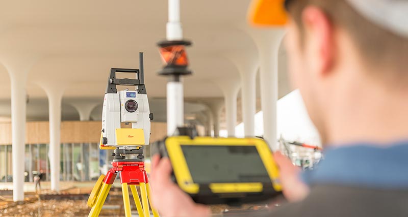 Leica iCON iCR80 on construction site with worker in front of it, holding a prism pole with a CC80 field controller.